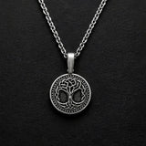 A silver pendant necklace featuring a circular tree of life design with Celtic knot details, displayed on a textured black background.