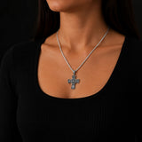 Silver cross necklace on a woman wearing a black top against a dark background