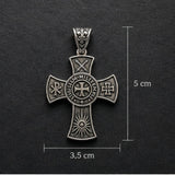 Silver cross pendant with intricate designs on a dark background, showing measurements.