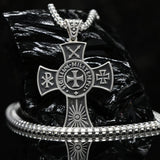 Handcrafted 925 sterling silver medieval cross necklace for men. A silver-toned metal cross pendant necklace with religious symbols and the words 'LIGHT MIGHTY CROSS' on the center, displayed on a black reflective surface with a matching chain and bracelet.