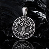 Handcrafted 925 sterling silver Tree of Life pendant with oxidized details. A silver pendant featuring an intricate Celtic knot tree design, displayed on a reflective black surface with a dark, textured rock in the background.