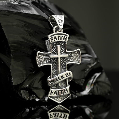 Silver cross pendant Faith with engraved text on a reflective surface