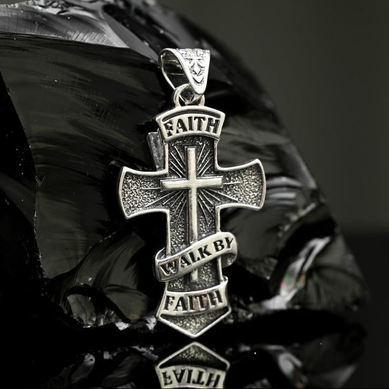 Silver cross pendant Faith with engraved text on a reflective surface