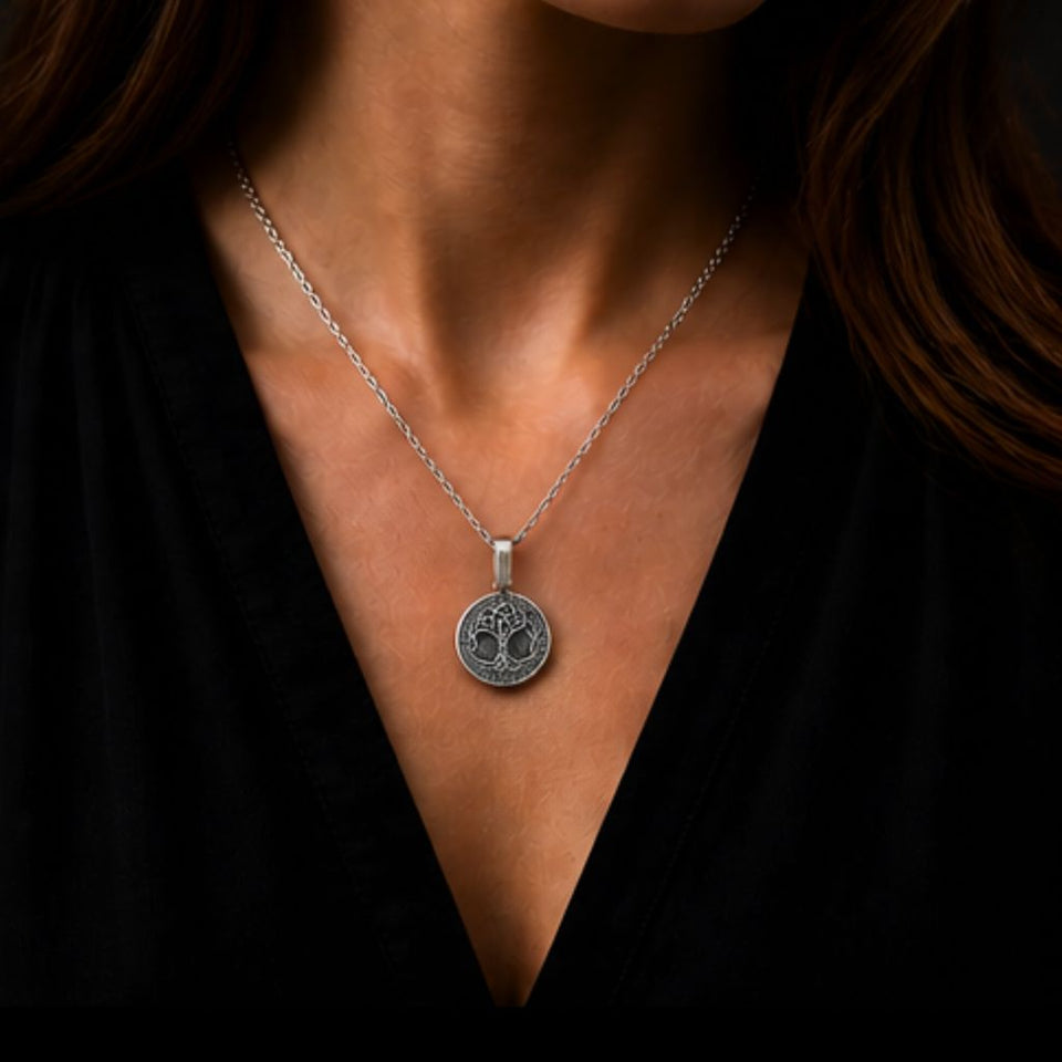 A close-up of a woman wearing a silver tree of life pendant necklace on a black top.