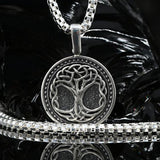 A 925 sterling silver necklace with a three of life pendant featuring a tree of life design, displayed on a black reflective surface with a black rock prop.