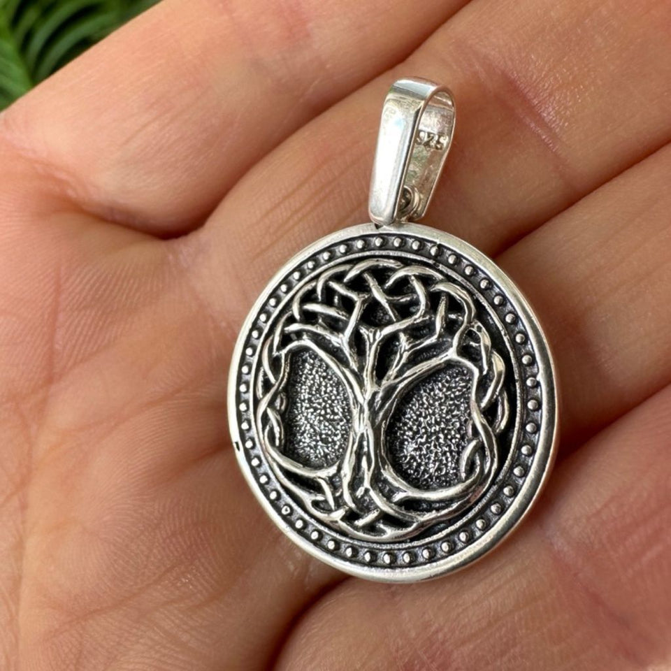 Detailed close-up of Norse Yggdrasil Tree of Life engraved silver necklace. A silver pendant with an intricate Celtic knot tree design, held in a person's hand to show scale.